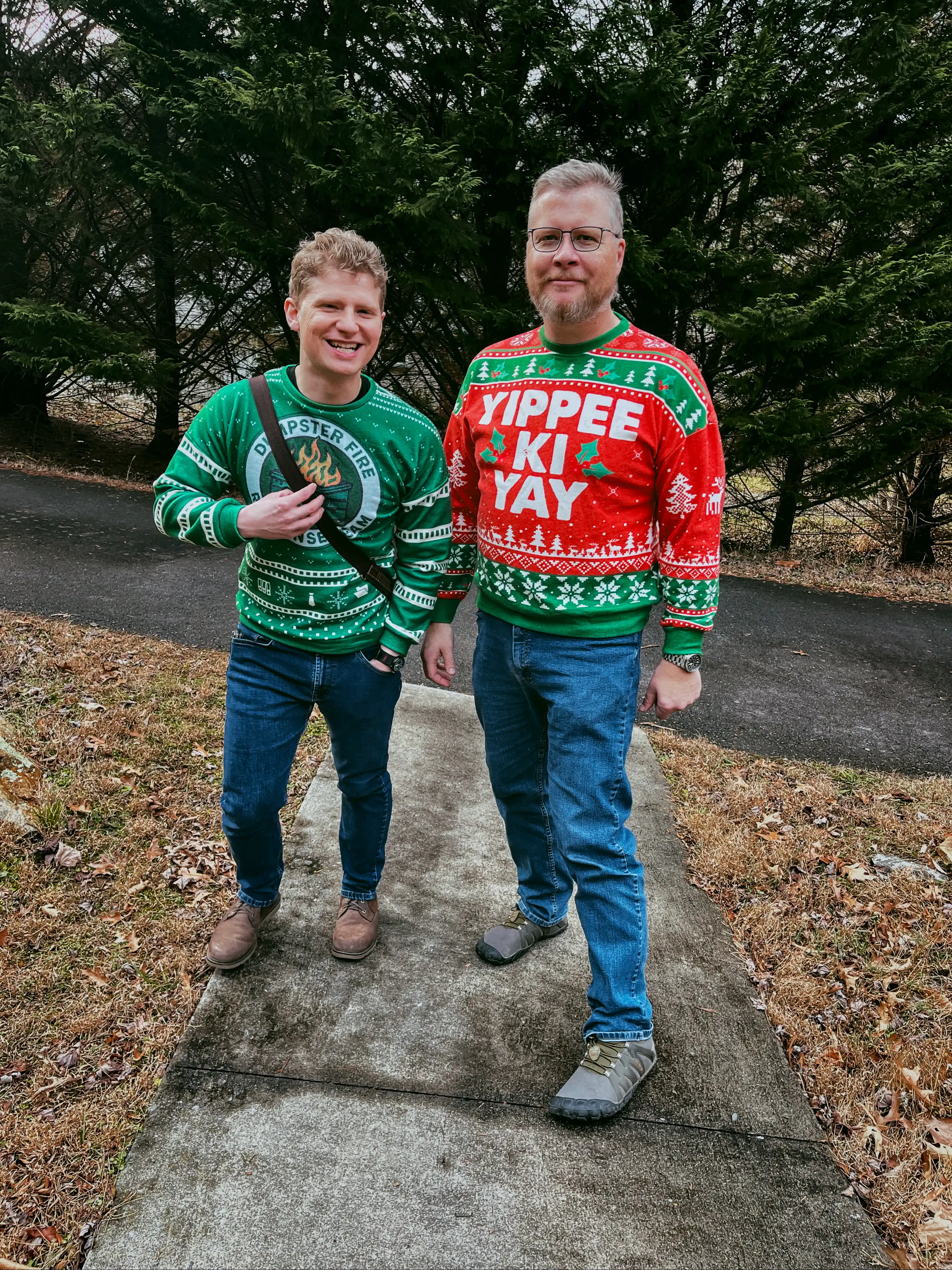 Two guys in ugly Christmas sweaters, one reading “Yippee Ki Yay” and one reading “Dumpster Fire”